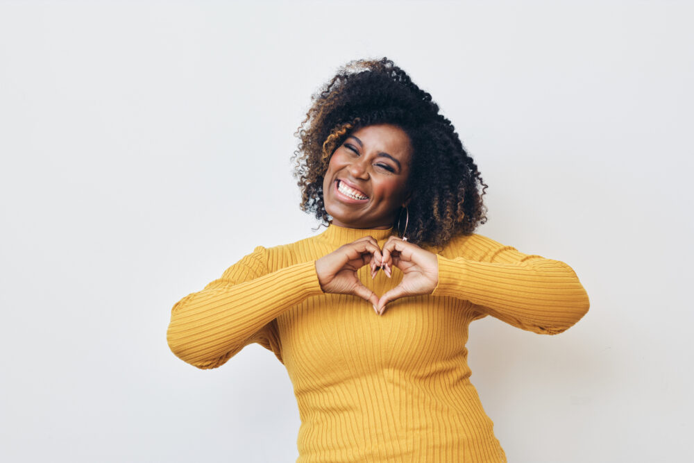 Personal branding photo of a woman making a heart shape with her hands, expressing warmth and authenticity