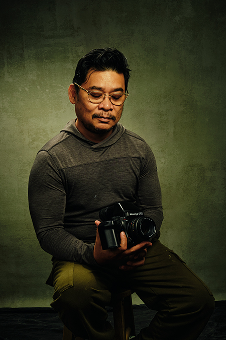 Photographer Portrait from Being in New York Series Portrait of a male photographer seated on a stool, holding a film camera with his eyes closed.